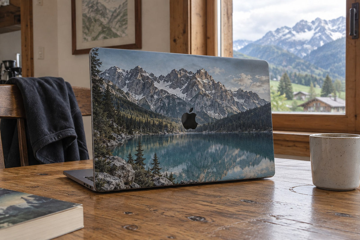 MacBook-Skin mit einem Bergsee-Foto als Motiv, auf einem Holztisch vor Bergpanorama. AI-generiertes Bild.